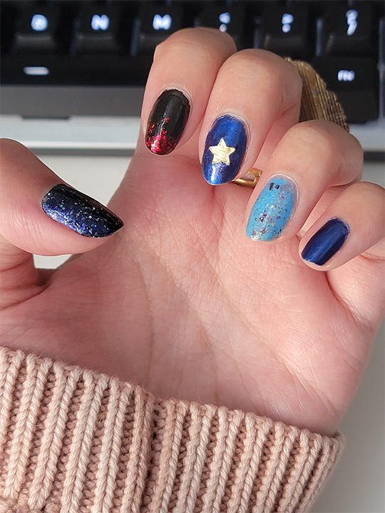 A photograph of nail art with mismatched blues and a red/black accent nail
