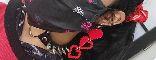 Close-up of accessory details: pixel heart health bar earrings, spiked choker, face mask.