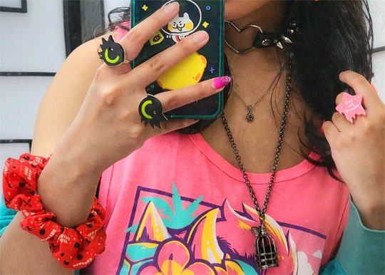 Close-up of accessories: layered necklaces, cartoon eye rings, star ring, and spiked heart choker.
