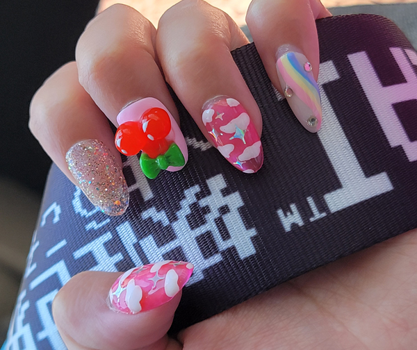 Close-up of mismatched pink nails with clouds, sparkles, a rainbow, and cherries.