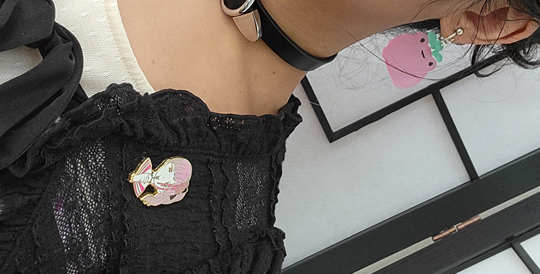 Close-up of accessories: strawberry frog earrings and anime girl enamel pin.