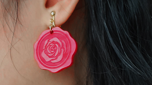 Close-up of a red acrylic wax seal earring with a rose pattern. It matches the red accents of the coordinate.