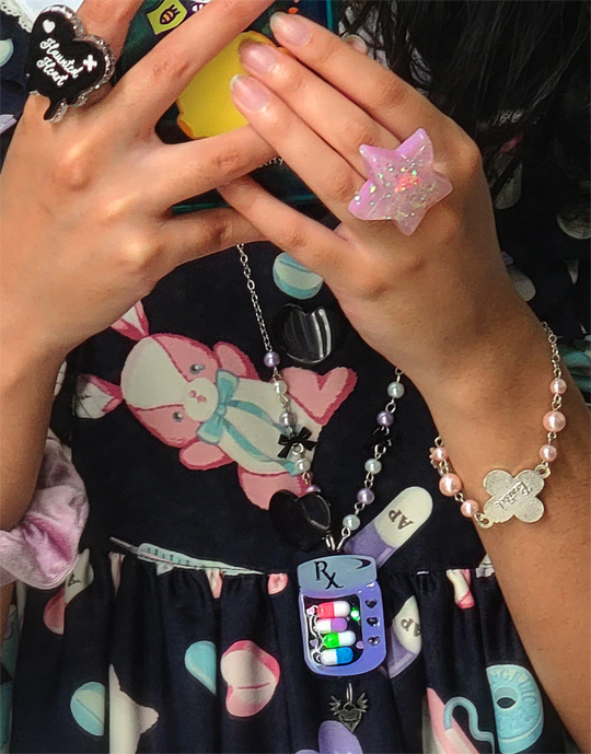 Close-up of accessories: heart and star rings,a colorful pill bottle necklace, and a bracelet.