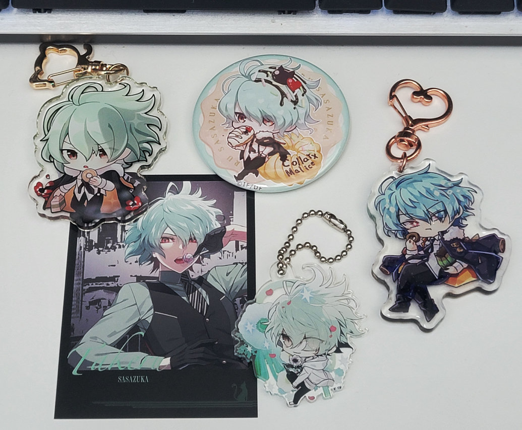 A photo of various keychains, a circular tin badge, and faux photocard of Sasazuka from the otome game Collar x Malice.