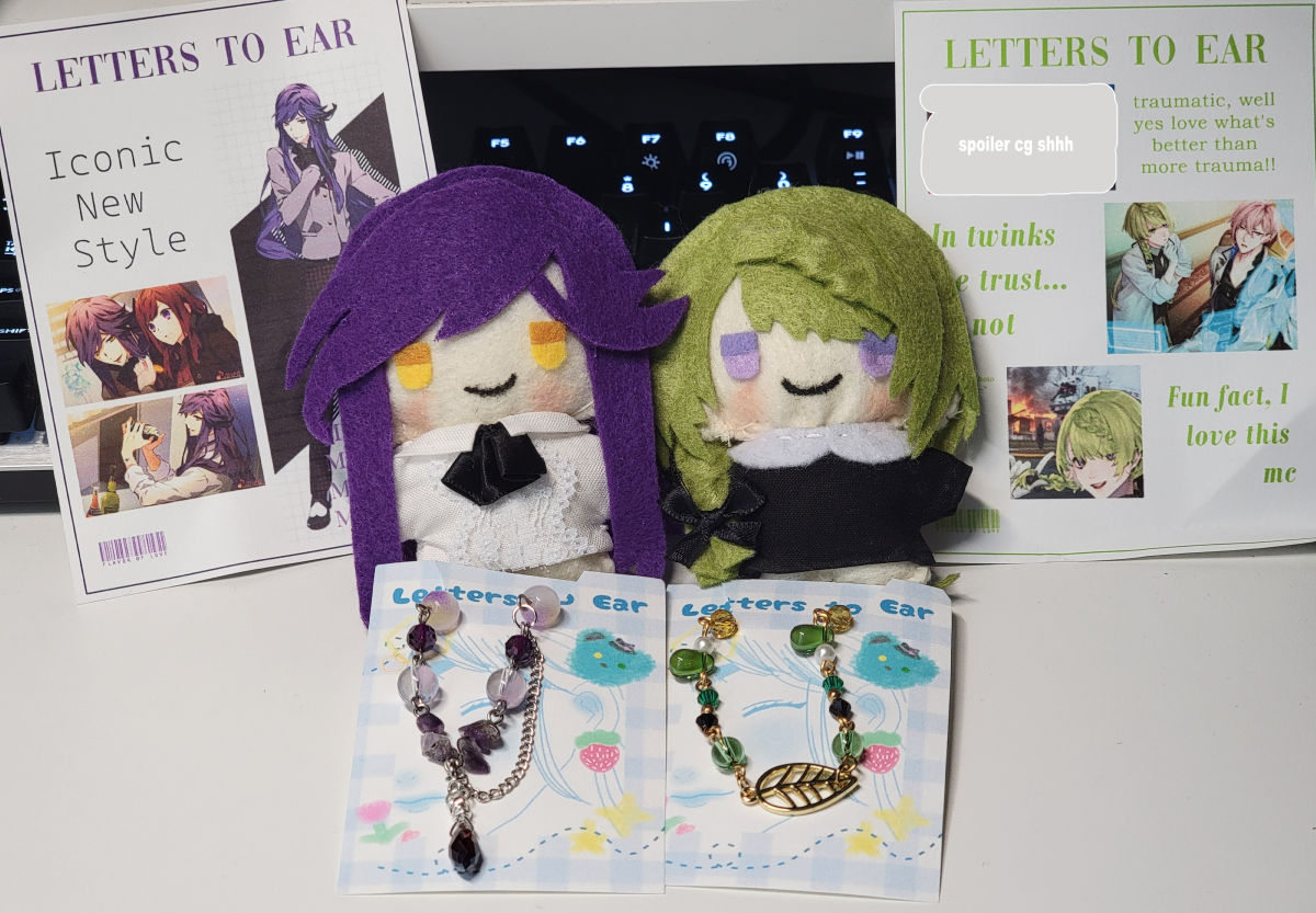 A photo of both plushes with their custom packaging and bracelets together